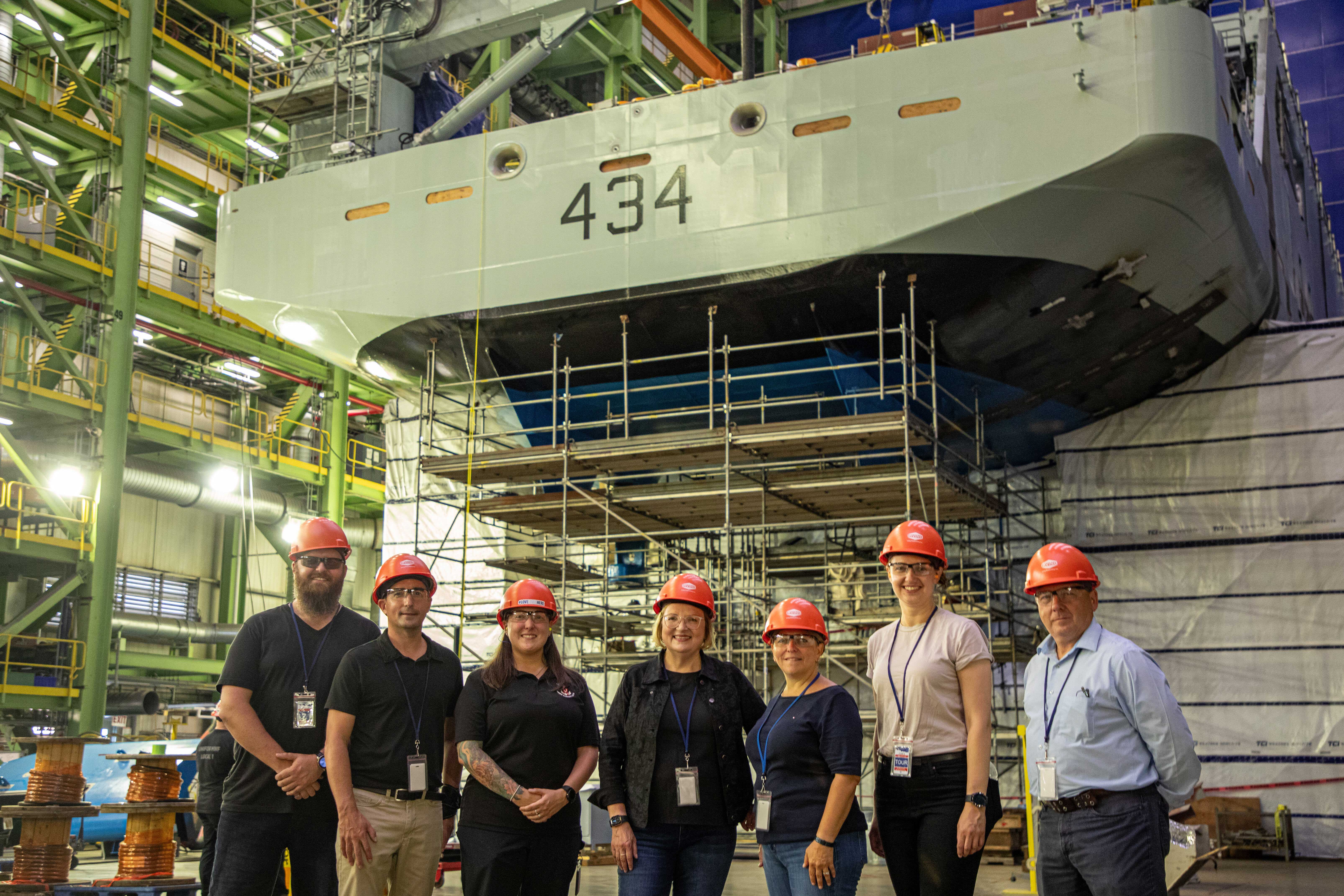 A group of seven standing in front of a stern module wearing hardhats at the Halifax Shipard