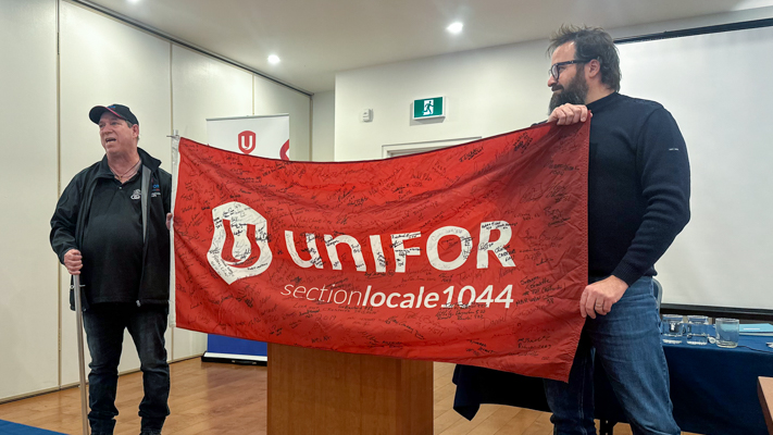 Two people standing holding a Unifor flag with signatures on it