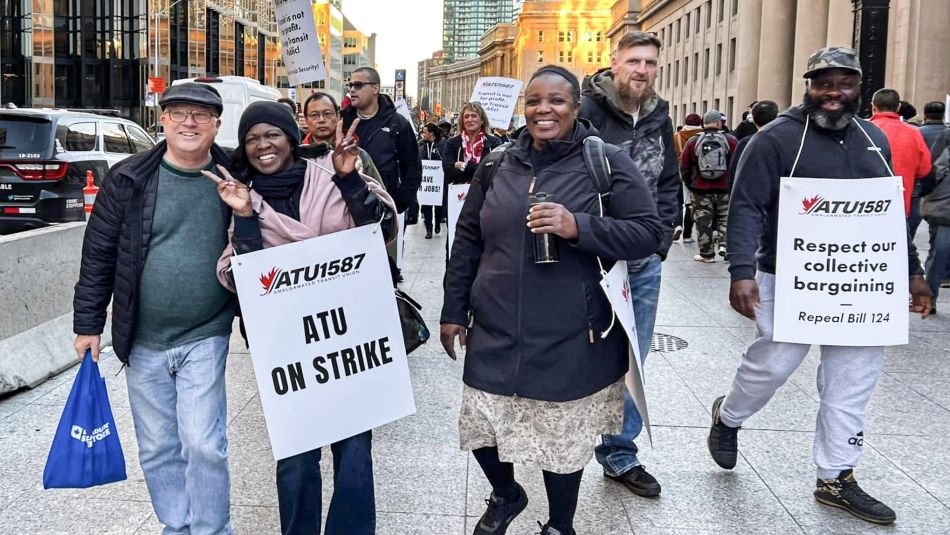 several people smiling and posing for a photo outside with ATU strike placards