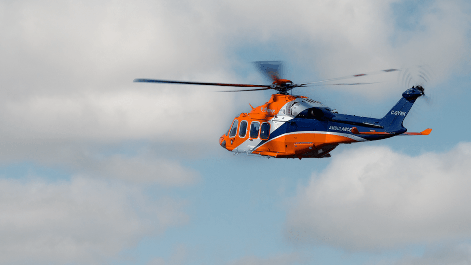 An Ornge helicopter flying in a cloudy sky.