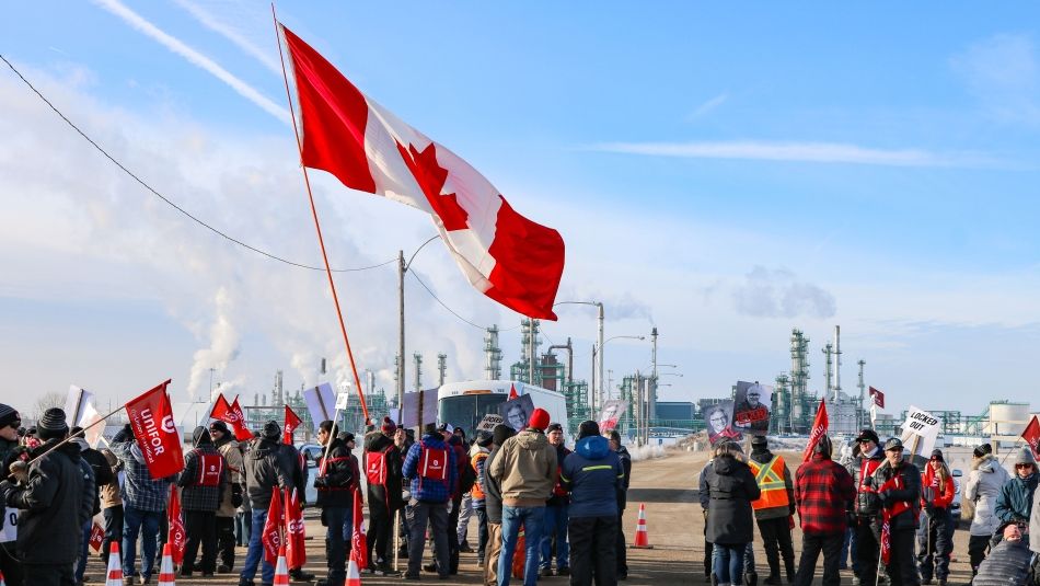 members holding a Canadian and Unifor flags on the picket line in Regina