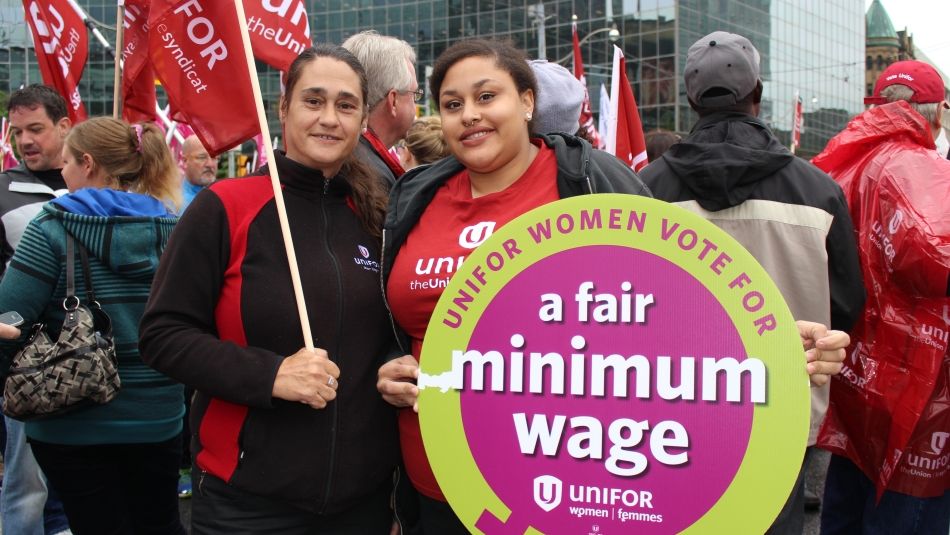 Deux membres d'Unifor, l'un tenant un drapeau et l'autre une pancarte demandant un salaire minimum équitable, lors du Rallye pour le travail décent à Toronto. 