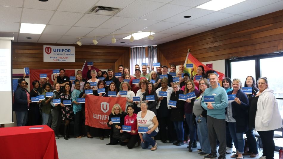 A large group of Unifor members hold cards pedging to vote in the Ontario Election.