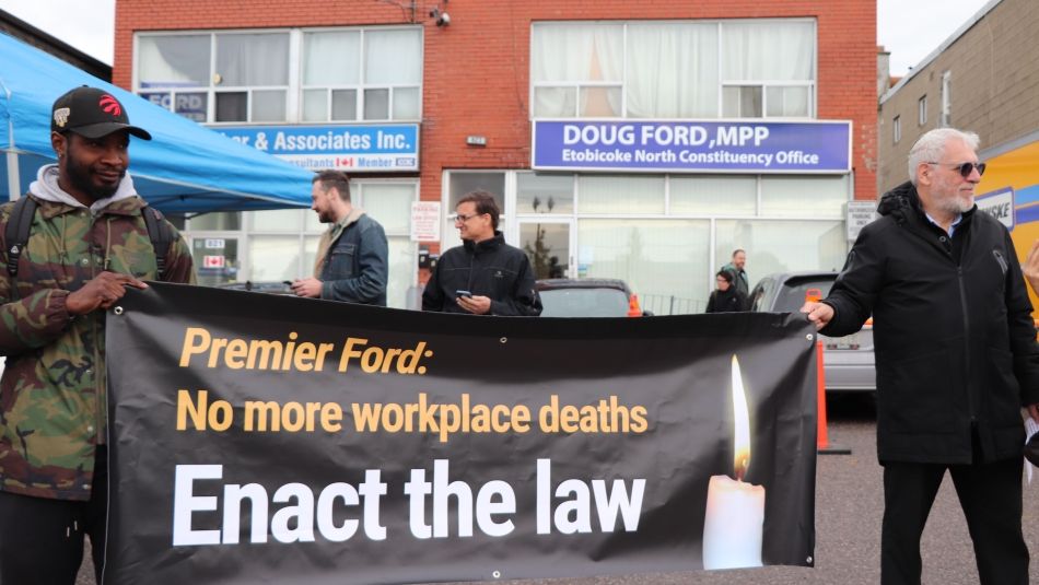 Activists hold a sign reading "Premier Ford: No more workplace deaths."