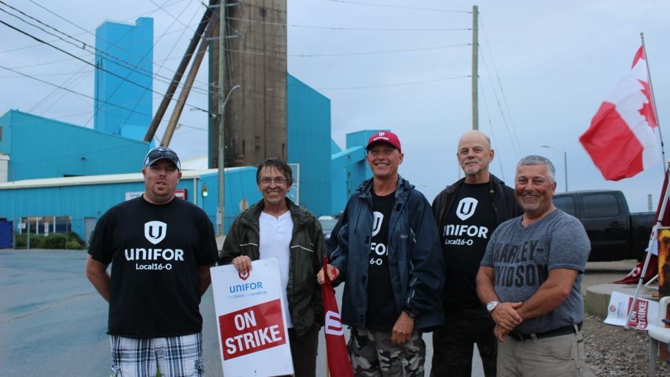 Five Unifor Local 16-O members stand on a picket line.