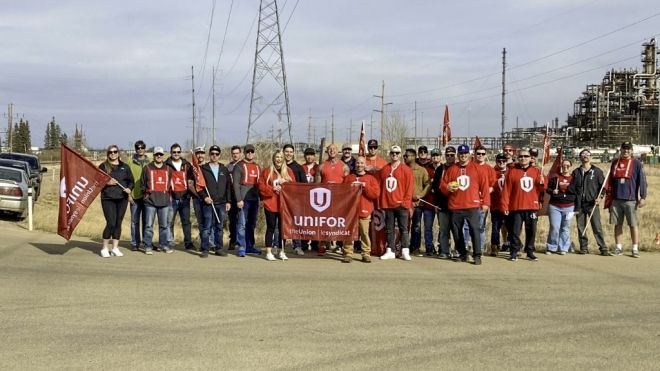 Large group of members posing in a group outside holding up a Unifor flag.