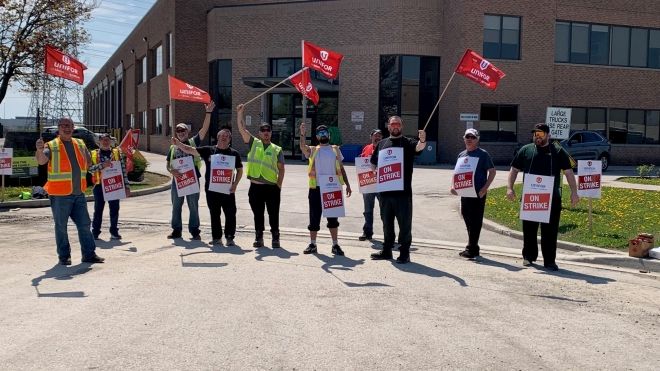 A group of people standing waving red Unifor flags