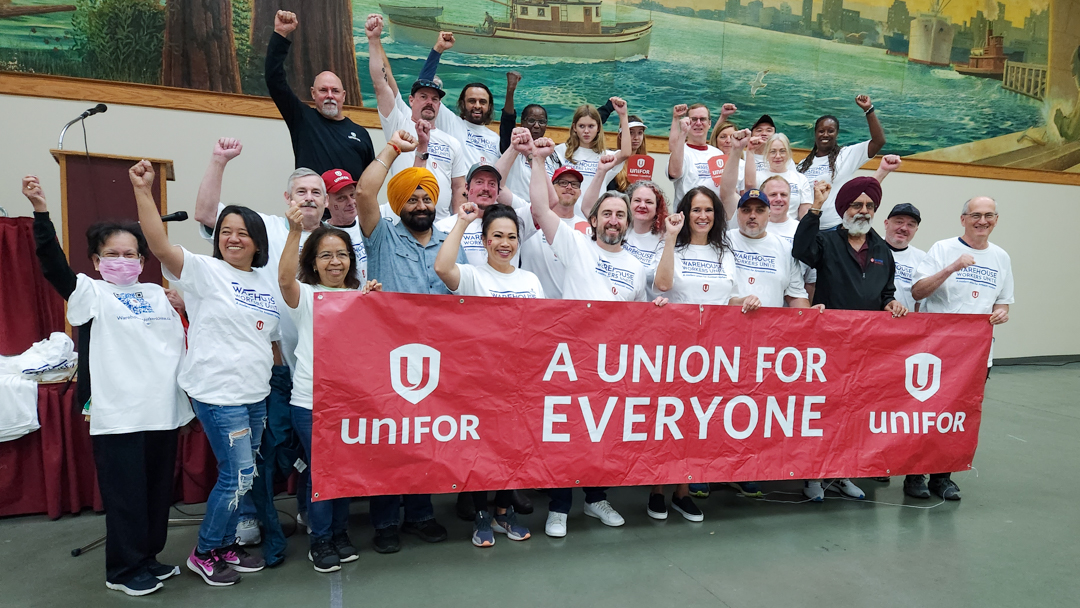 Group of approximately 30 people posing for photo with fists in the air wearing white t-shirts and holding a red banner that reads A union for everyone.