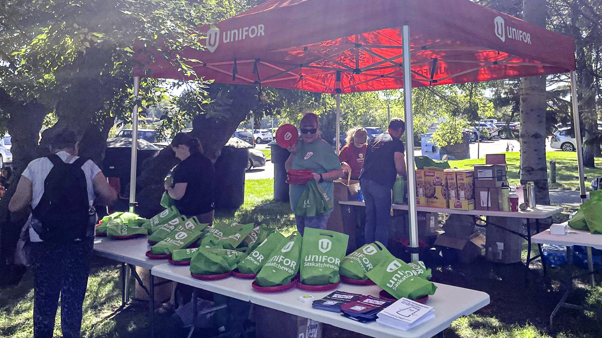 Three people standing under a canopy with tables loaded with gift bags