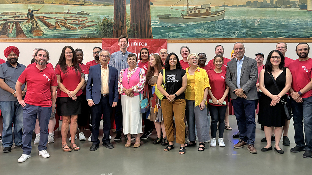A group of people standing in front of a Unifor flag