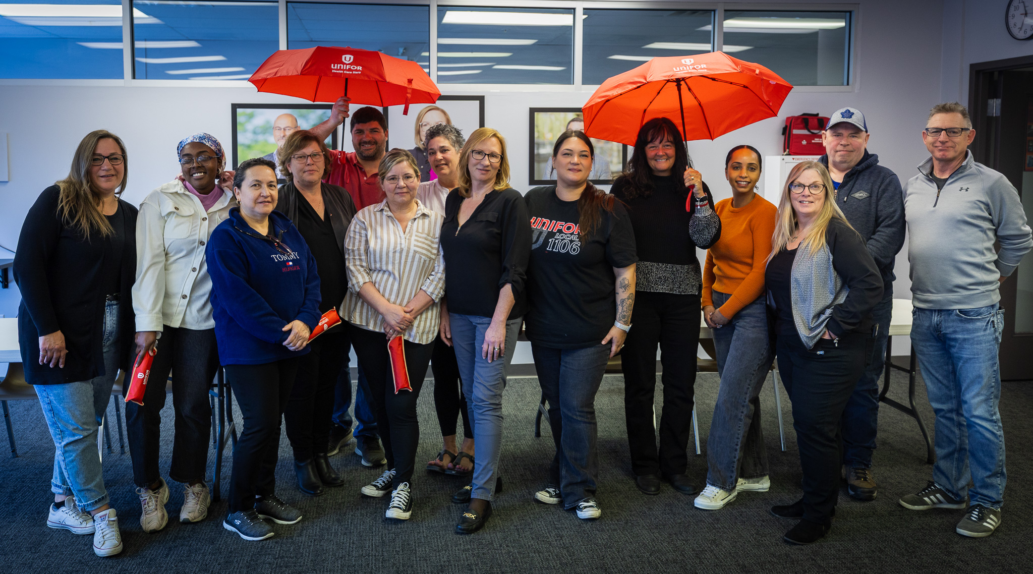 A large group of people posing two are holding up red umbrella's 