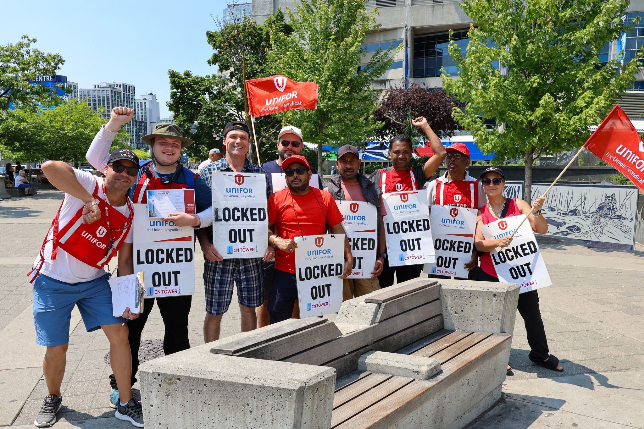 Nine people holding locked out placcards, red Unifor flag and shirts