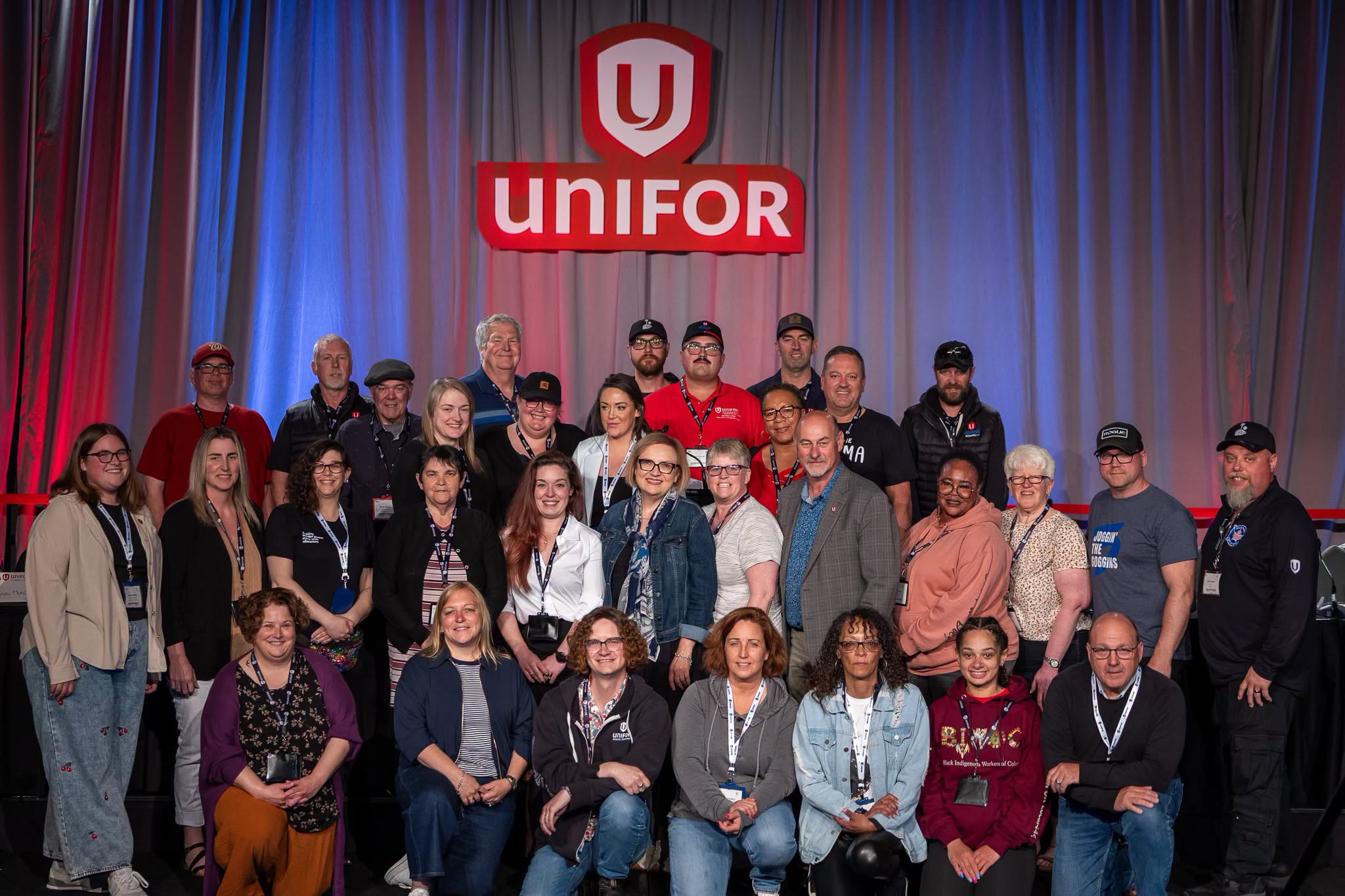 A large group on stage infront of a lit curtin and Unifor Logo