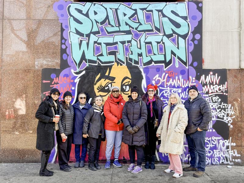 Dix personnes posent à l'extérieur devant une grande œuvre d'art de rue sur laquelle on peut lire "Spirits within" ("Les esprits à l'intérieur").