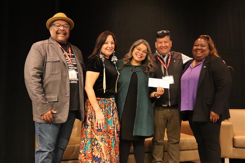 Five people on stage one person is holding up a cheque