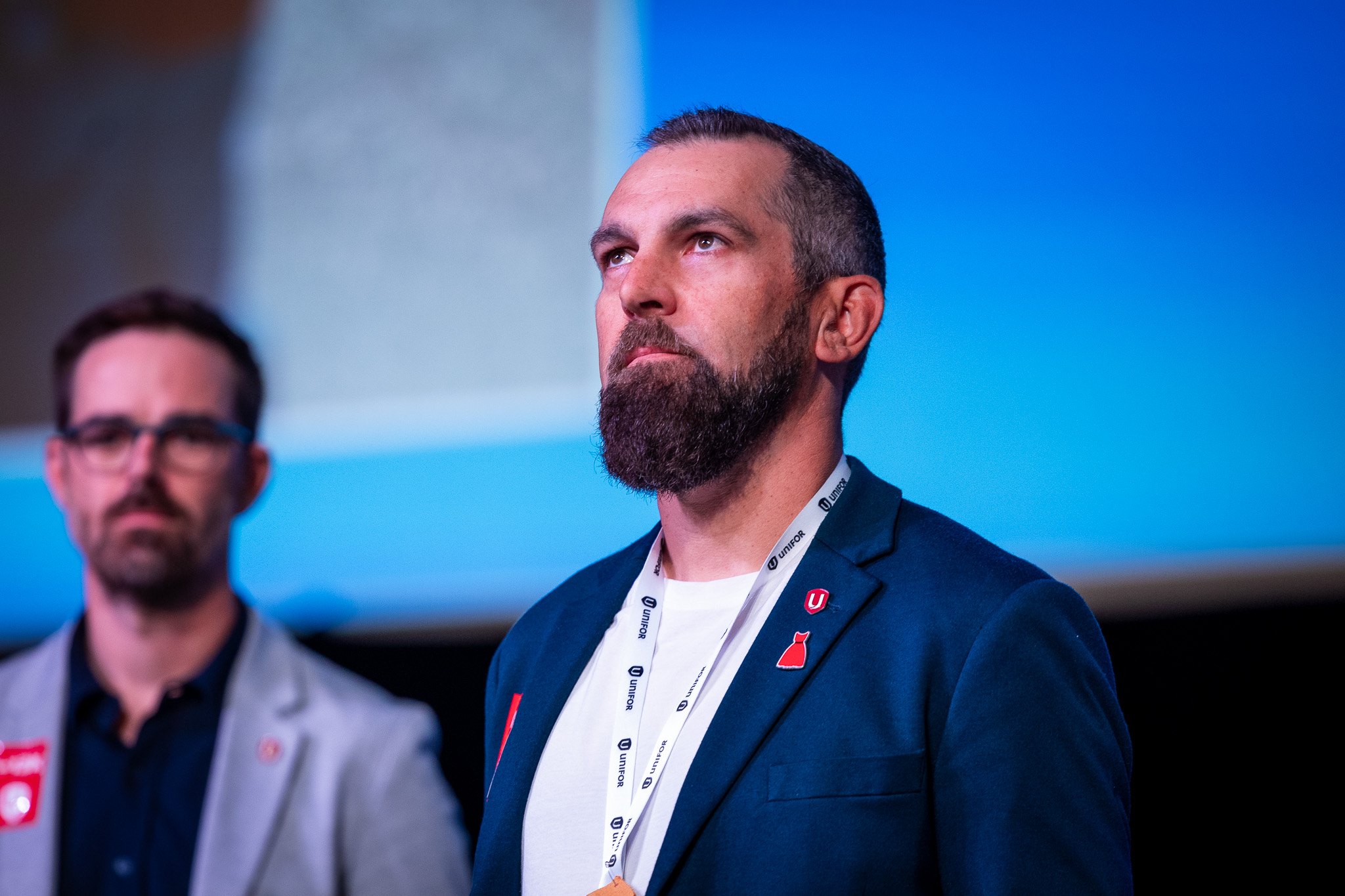 A man in a white shirt and blue jacket on stage with a digital background