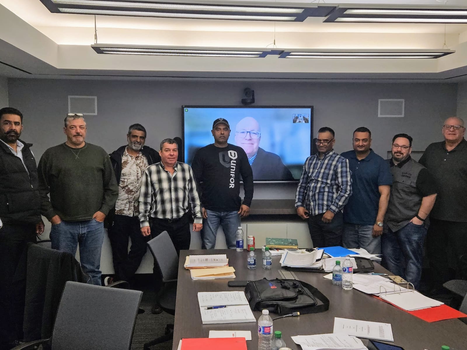 Nine men standing in front of a boardroom presentation screen