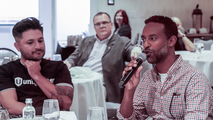 One person seated speaking on a mic while another watches