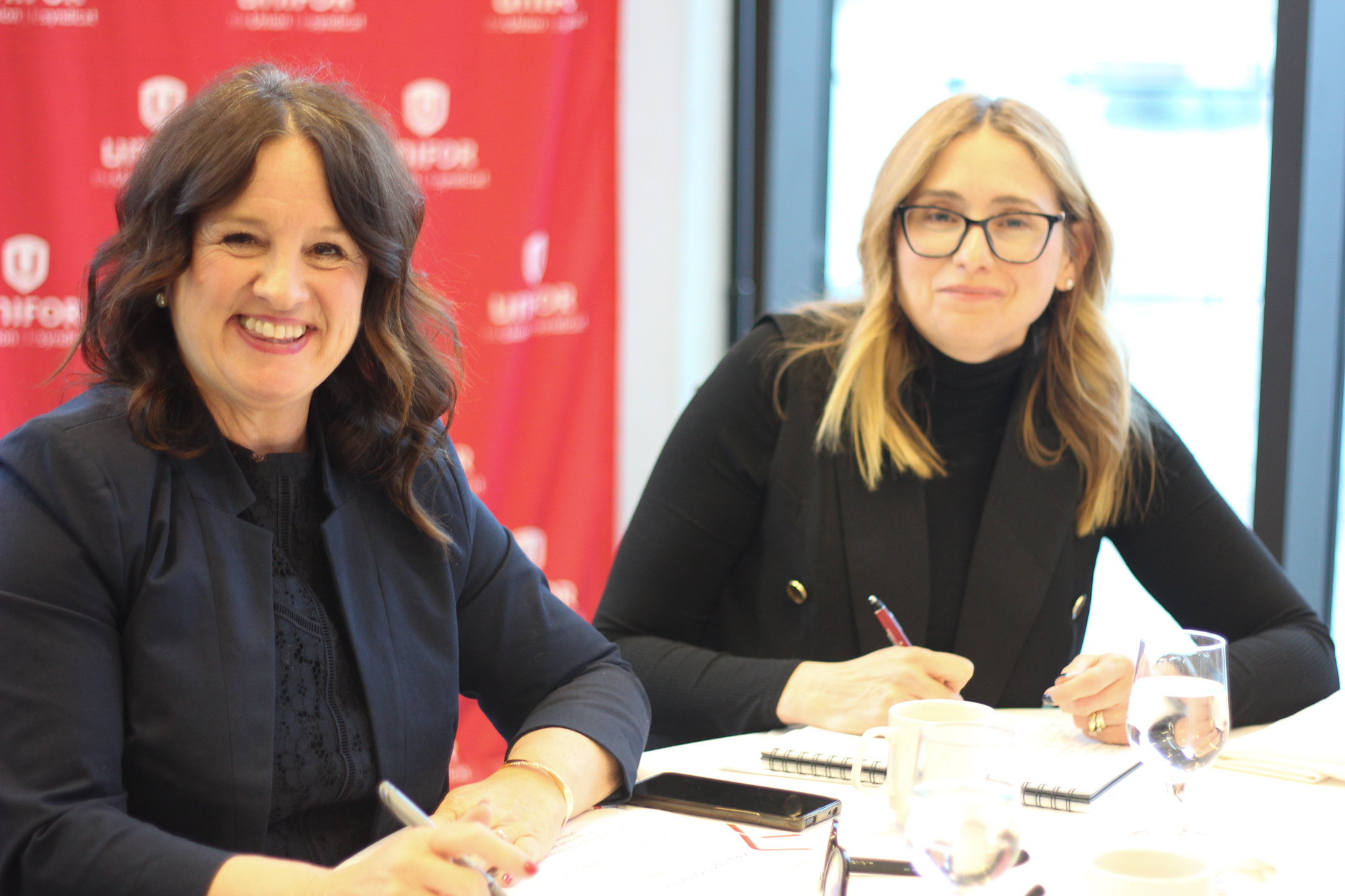 Two women smiling at the camera in front of a Unifor backdrop