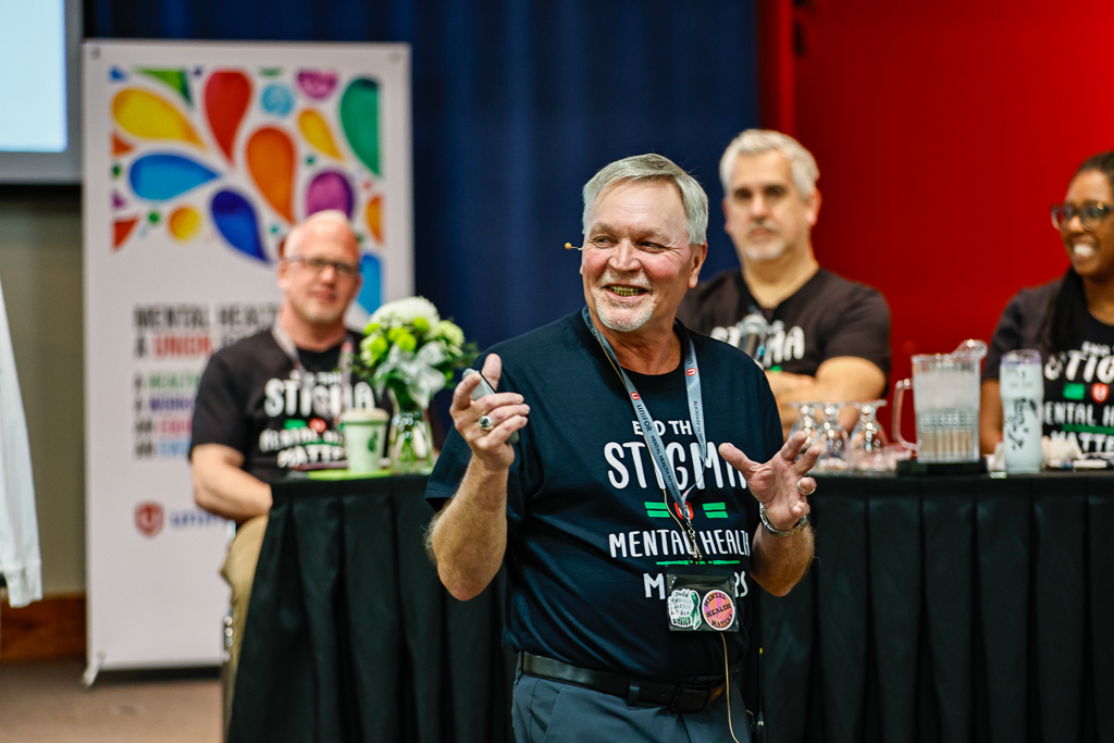 Three men stadning at the front of a room one is talking through a headset