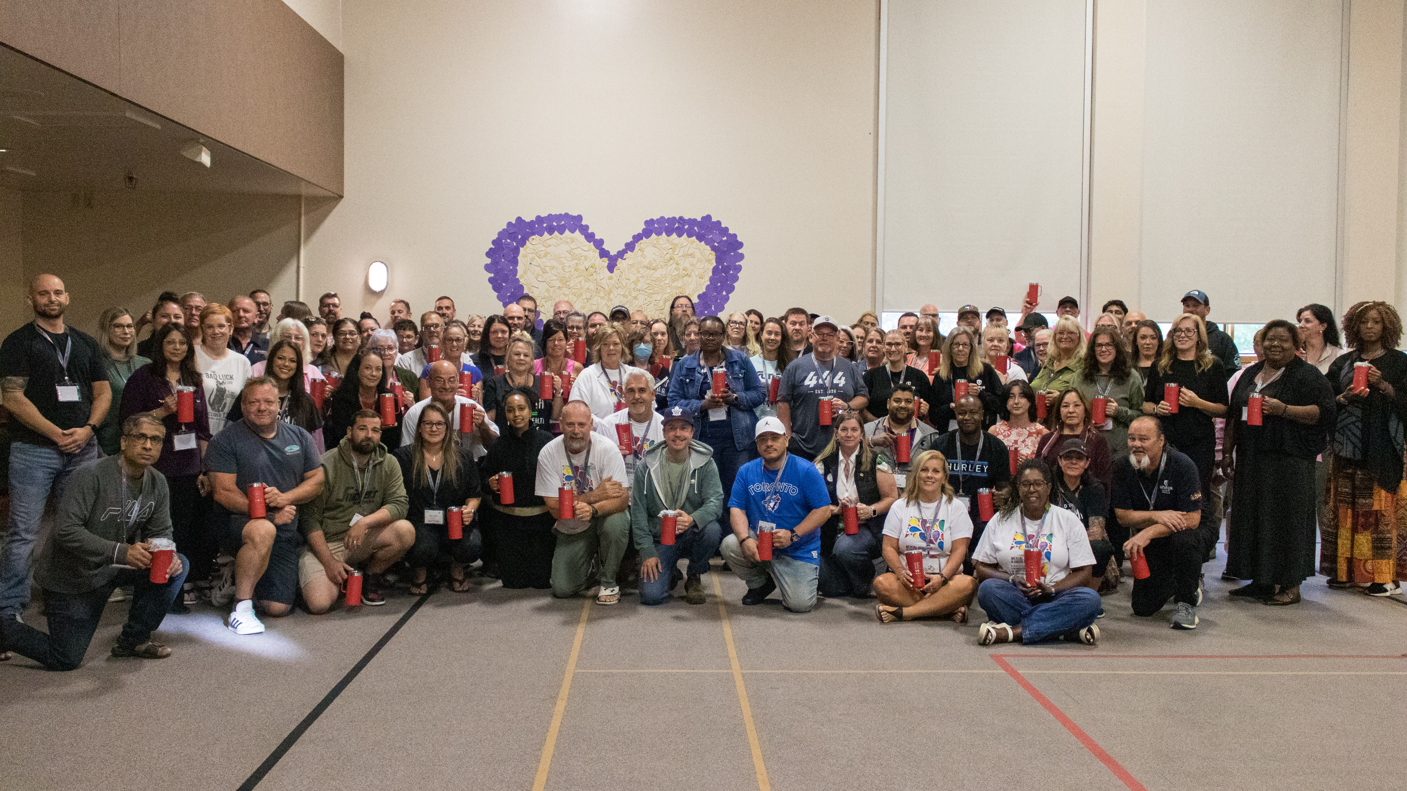 A large group photo in front of a giant purple heart on the wall behind