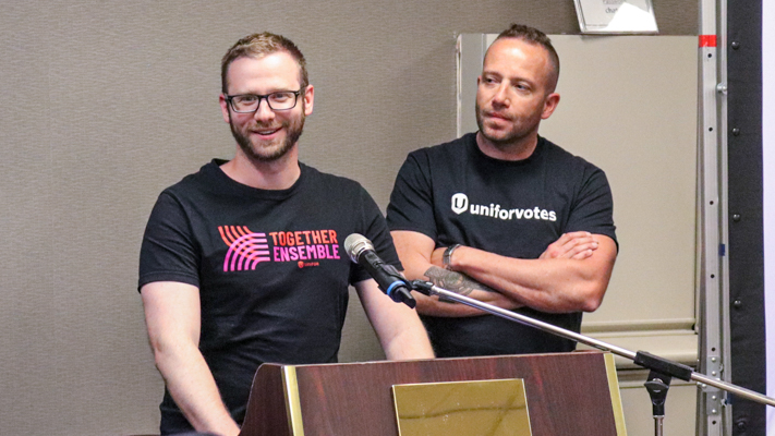 One person speaking at podium while another person nearby watches