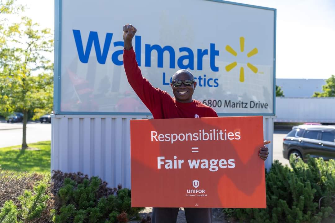 A man stands in front of an exterior Walmart sign holing up a placcard