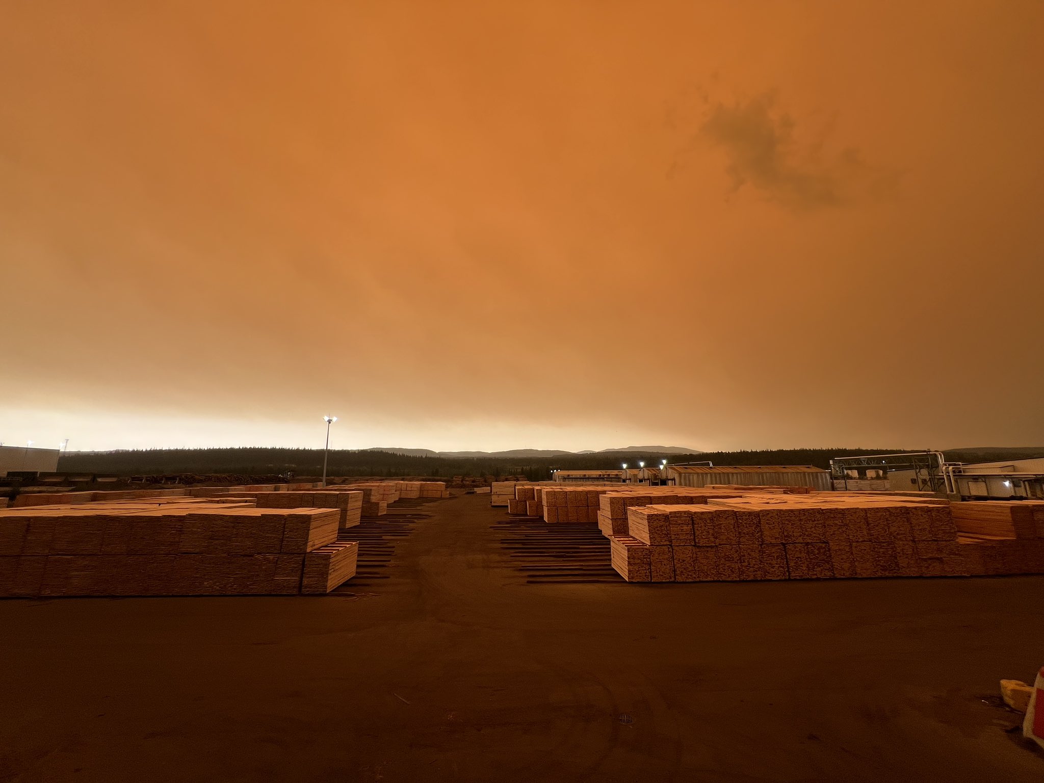 A lumberyard is illuminated by a hazy orange sky caused by wildfire smoke.
