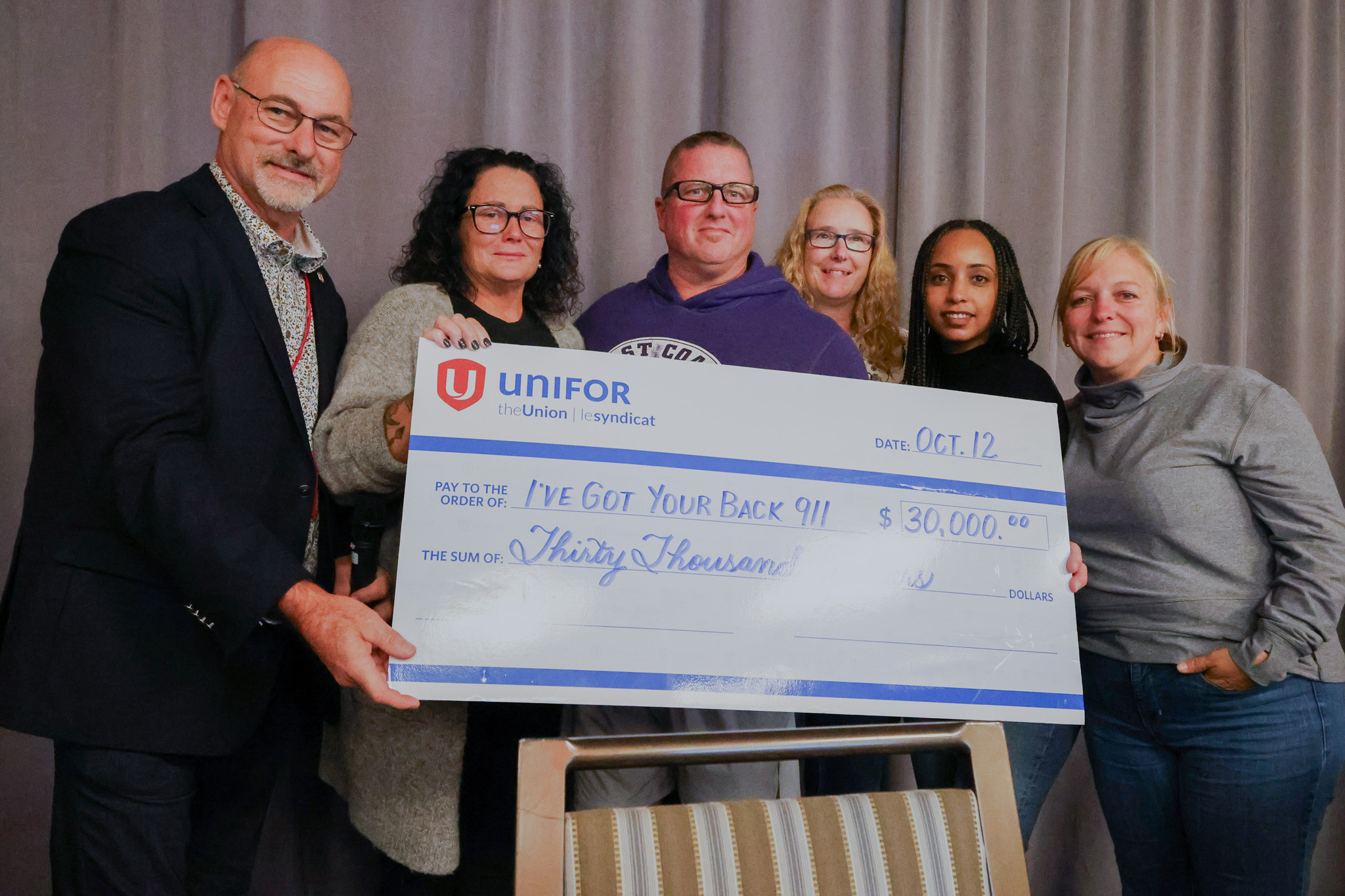 Six people hold up a oversized cheque