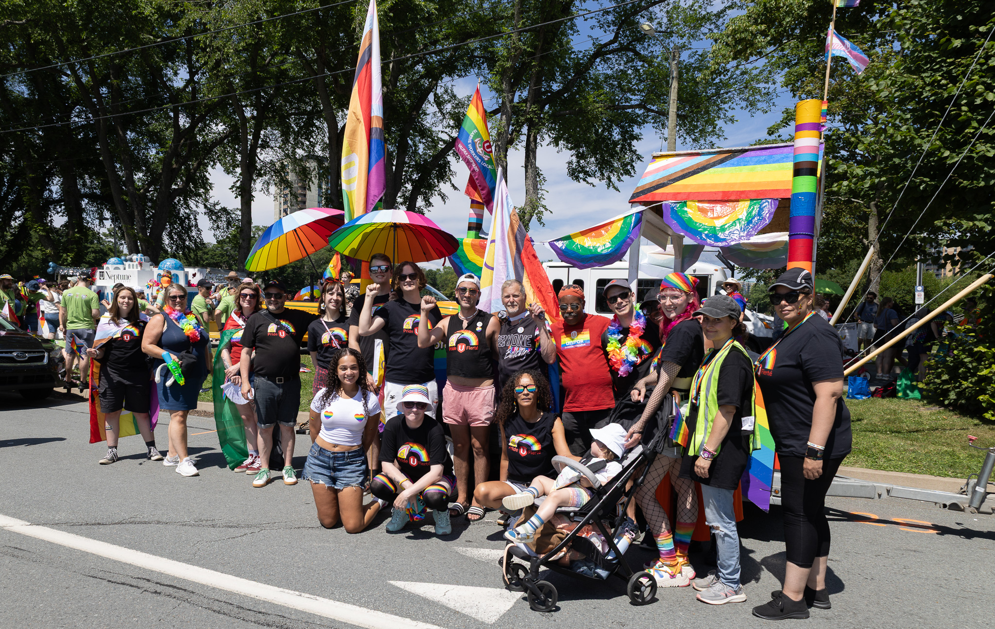 A group of people in the street holding pride flags and signs supporting unions and LGBTQ+ rights.