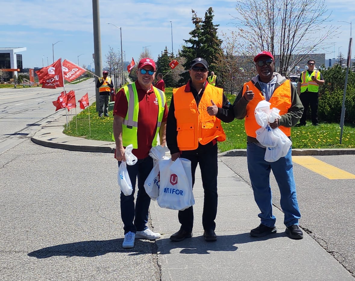 Three men wearing safety vests holding Unifor bags