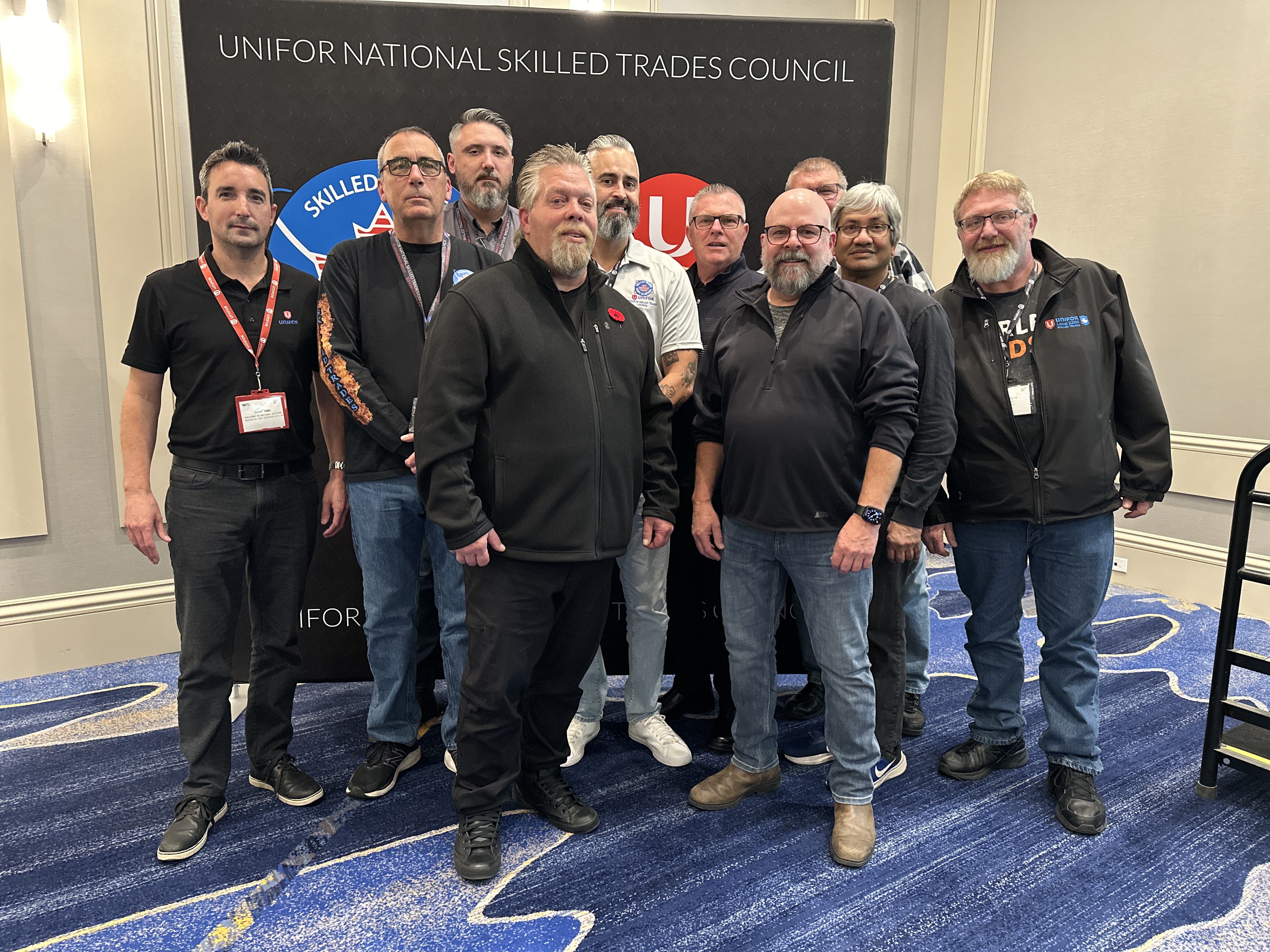 a large group of men standing in front of a pop up banner. 