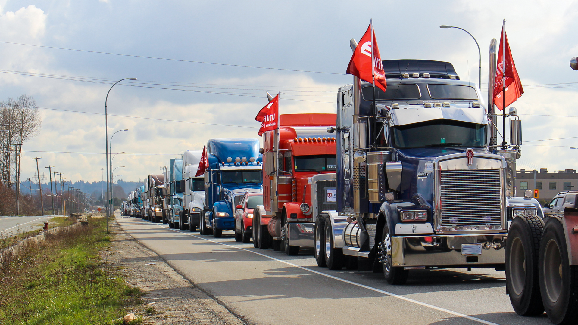 Long convoy of tractor trailer trucks, some with with Unifor flags