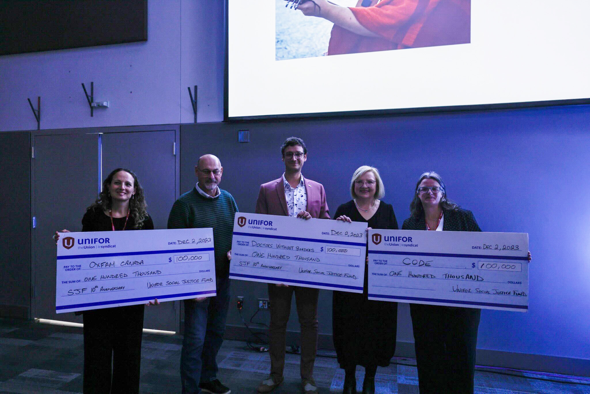 Five people holding up three giant cheques