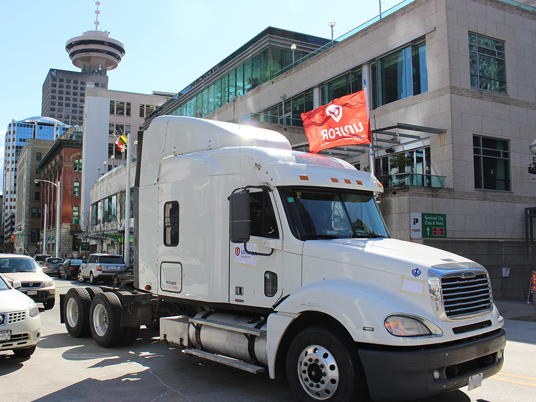 White tractor trailer in downtown Vancouver with a Unifor flag