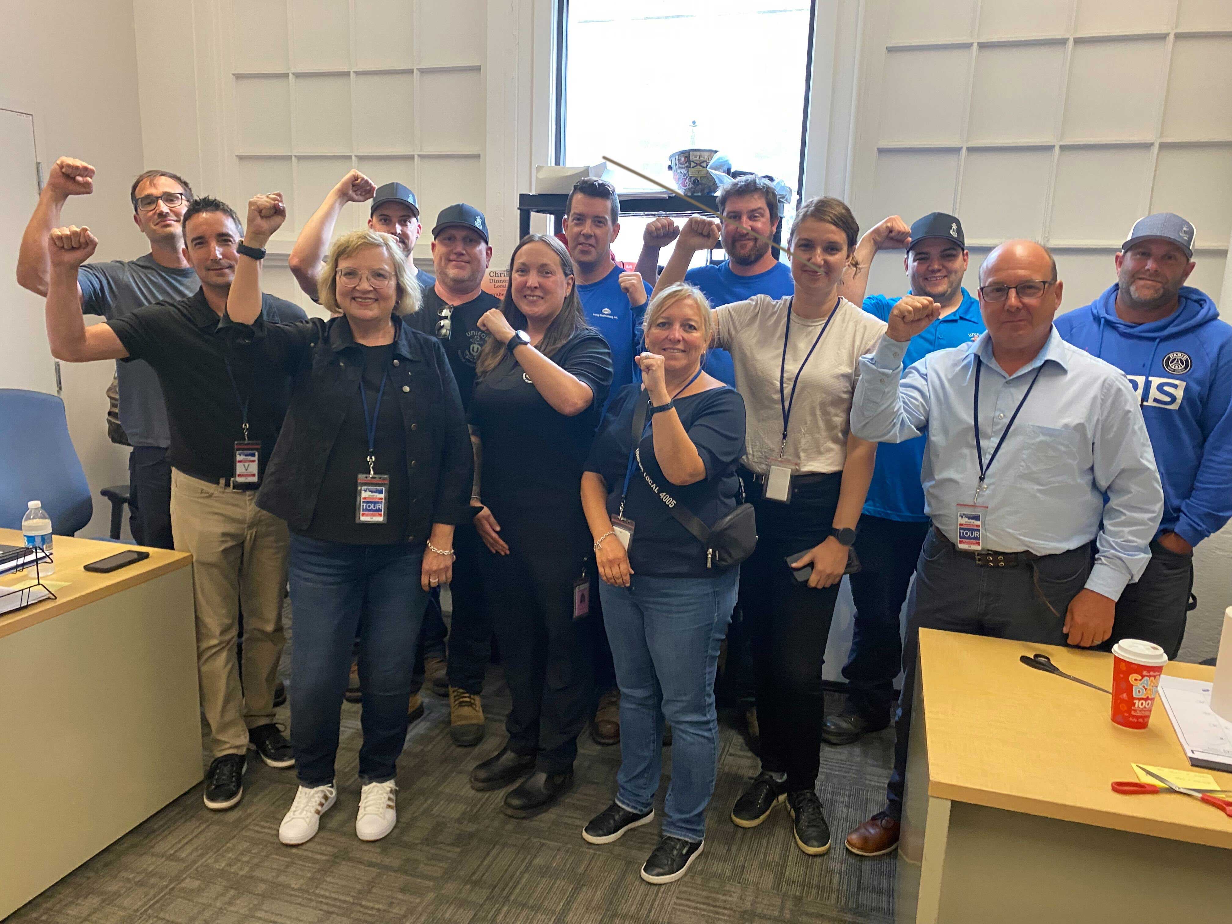 A group of Unifor Leadership and members from the Halifax Shipyard posing smiling with their fists raised.