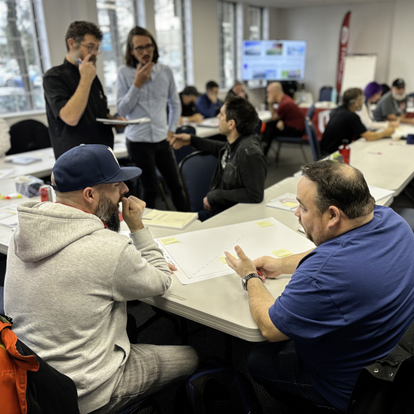 Unifor members Two seated people in dialogue with two standing people nearby in a room full of people seated at tables.