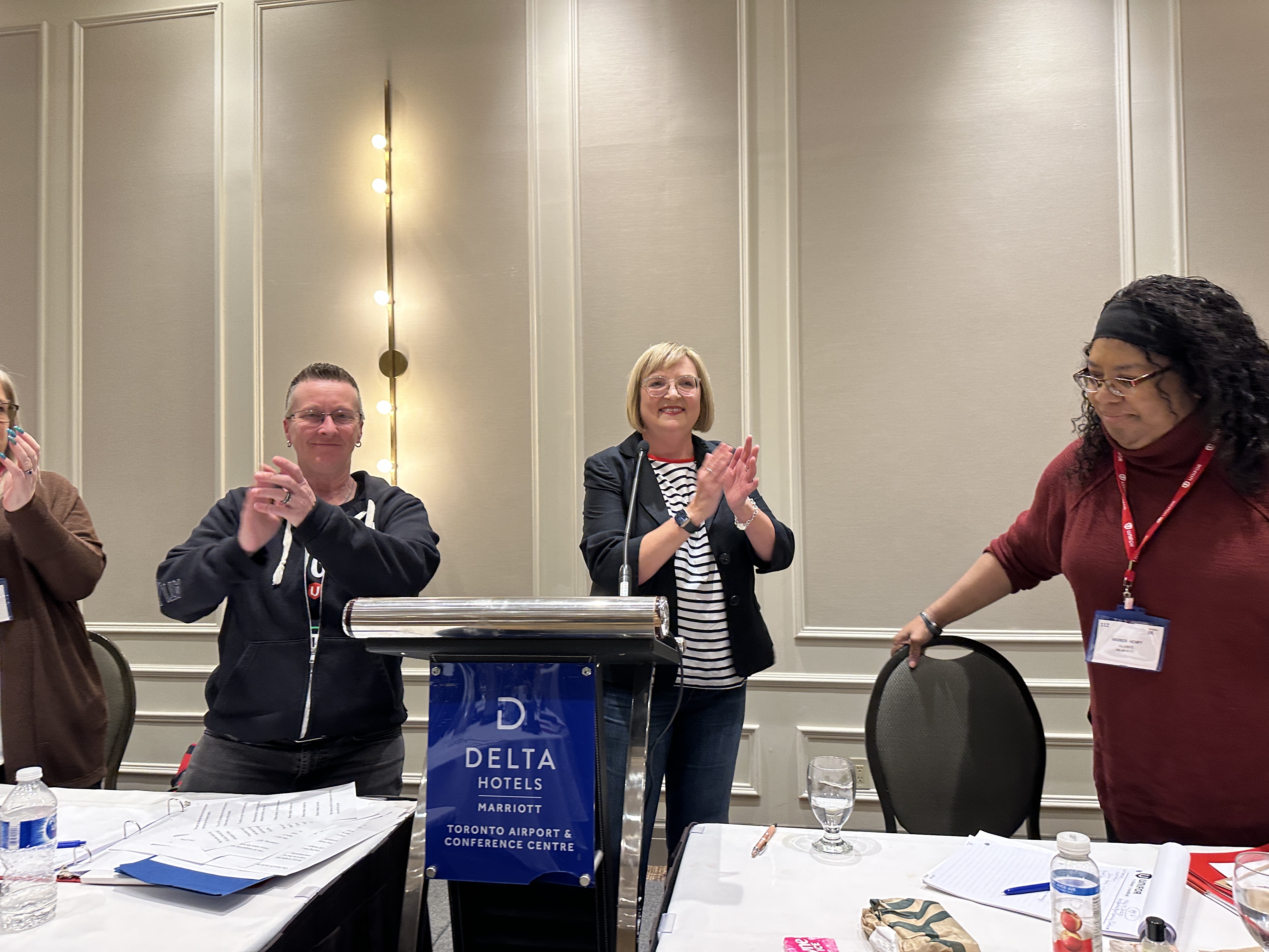 Two women and a man stand behind a podium clapping