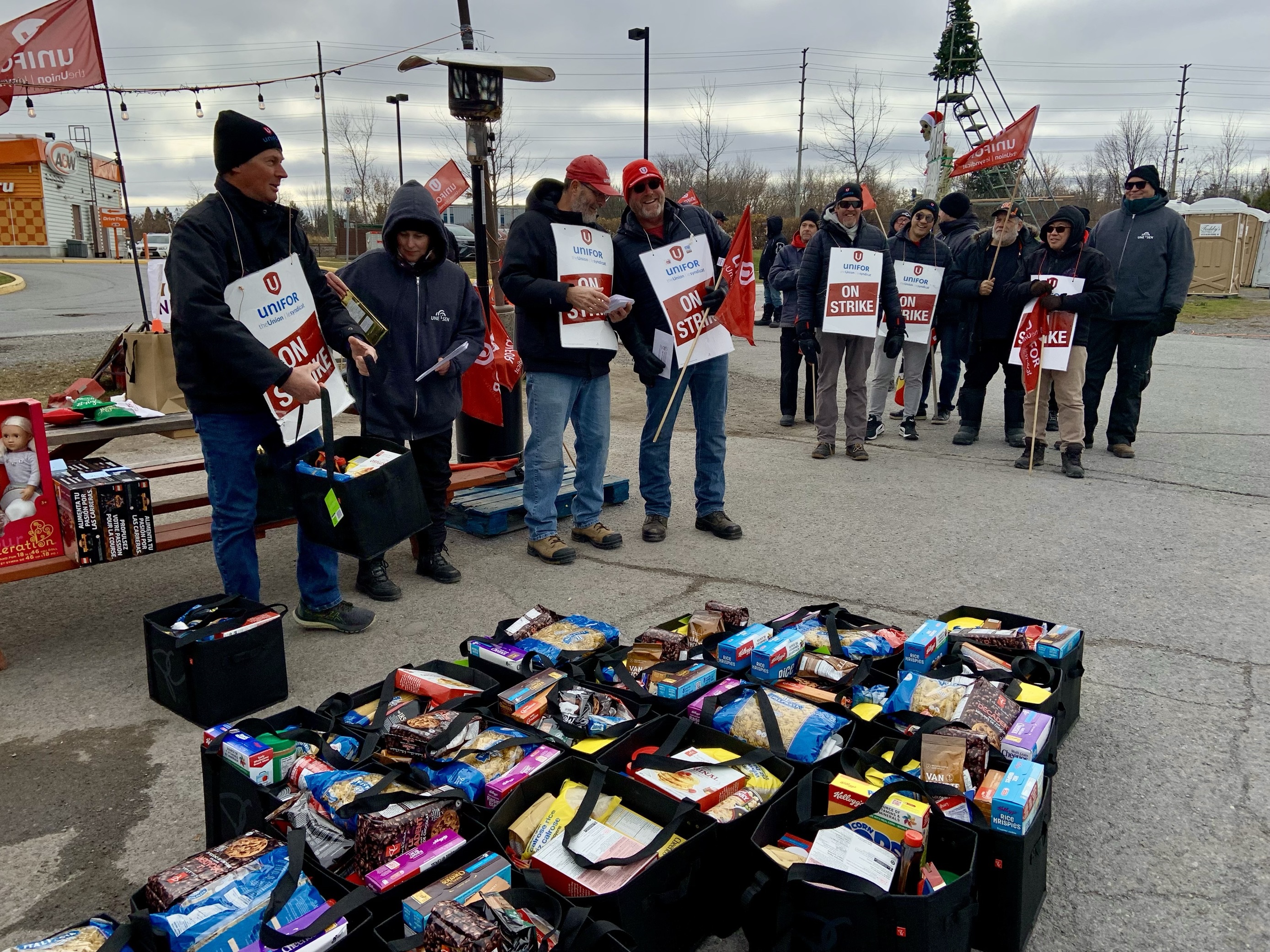 Striking workers wearing &quot;on strike&quot; signs stand outside, gift bags line the ground.