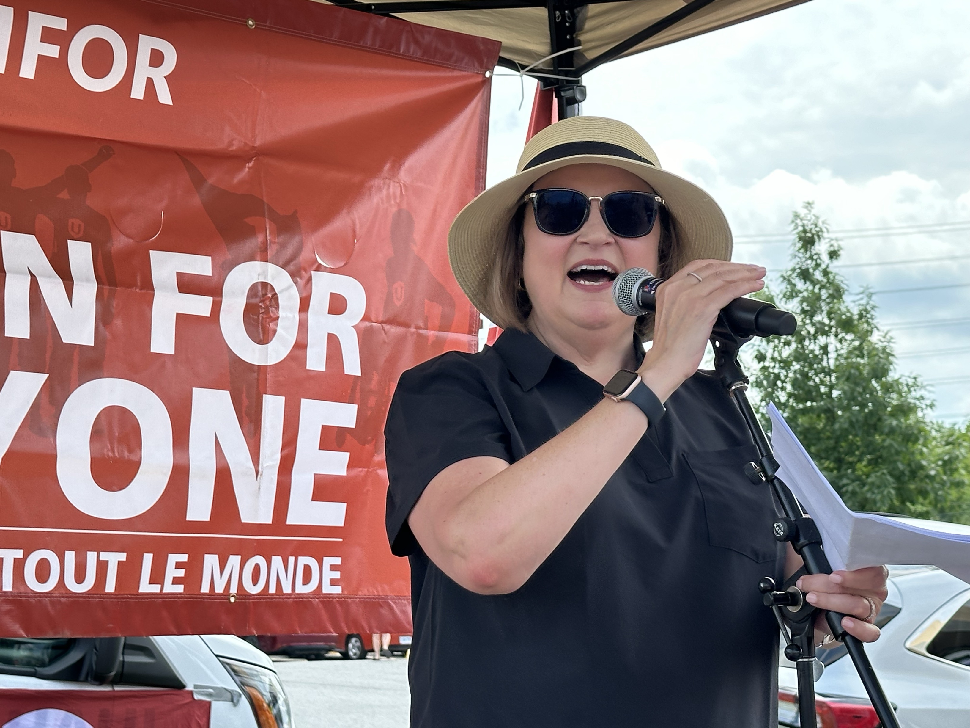 women speaking with microphone with unfor for one sign in background