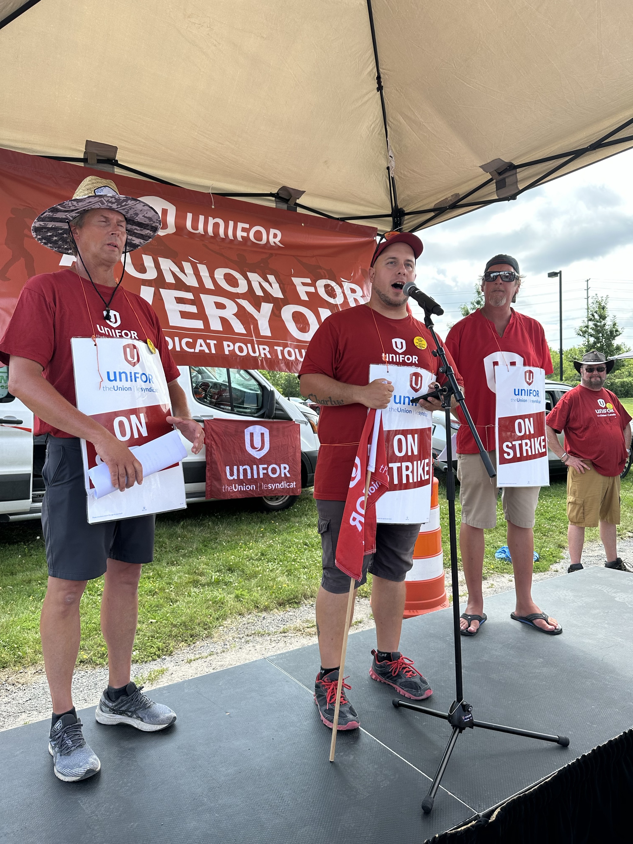 3 people in red shirts on stage with unifor union for everyone in the background