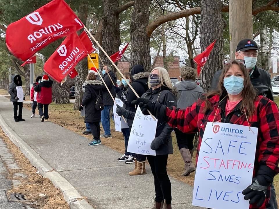 Women holding signs and Unifor flags on a picket line