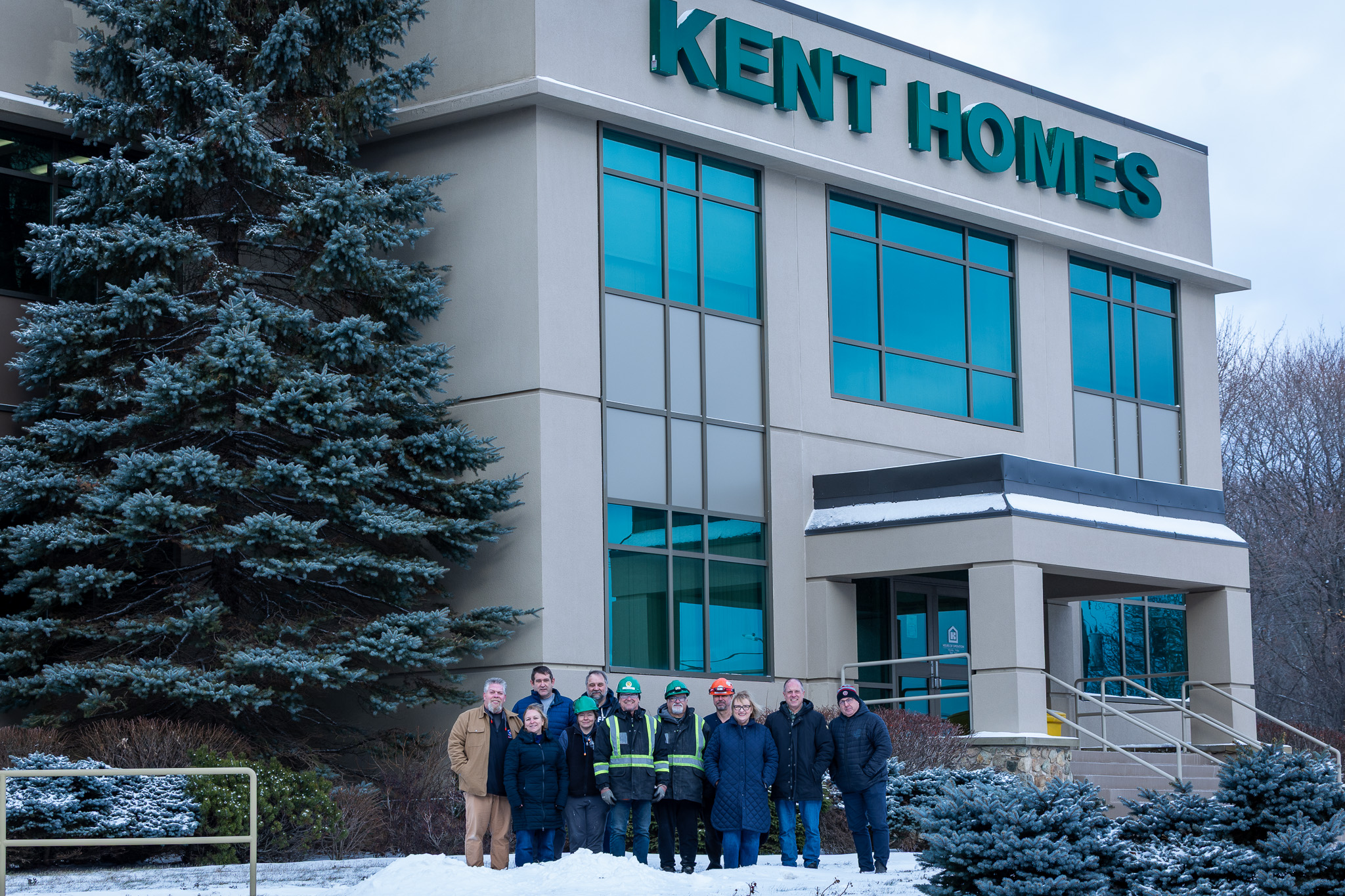 A group of people stand in front of a building with a sign that reads "Kent Homes"