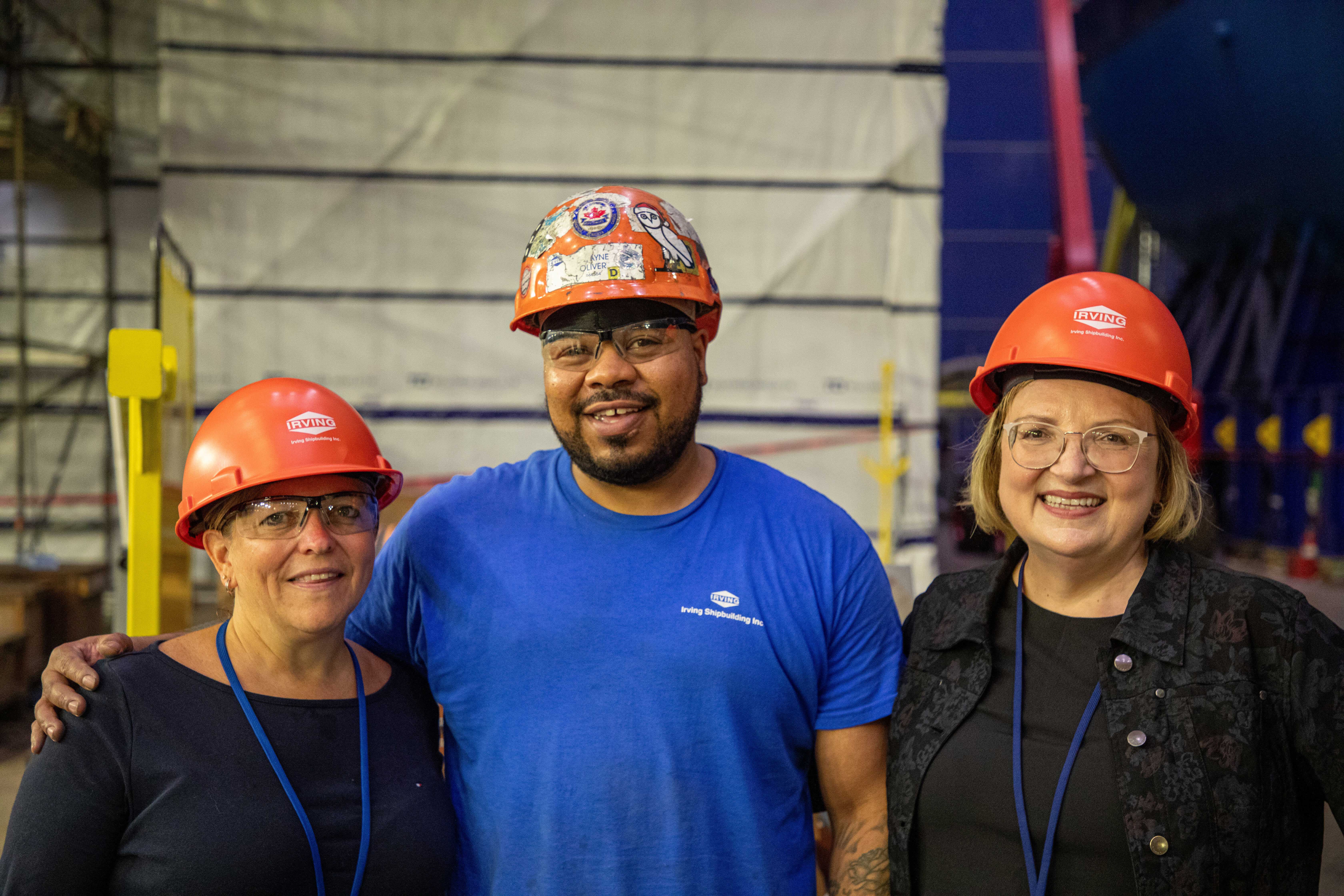 Lana and Jenn at posing with a member wearing hardhats smiling.