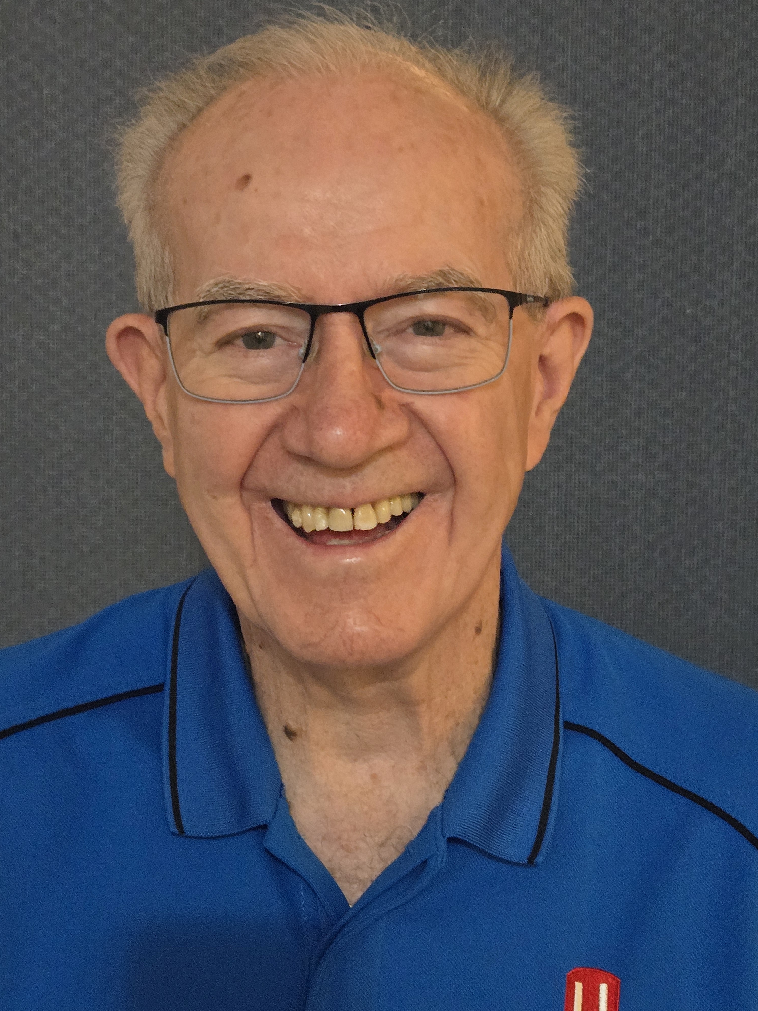 A photo of an older man wearing a blue shirt smiling.