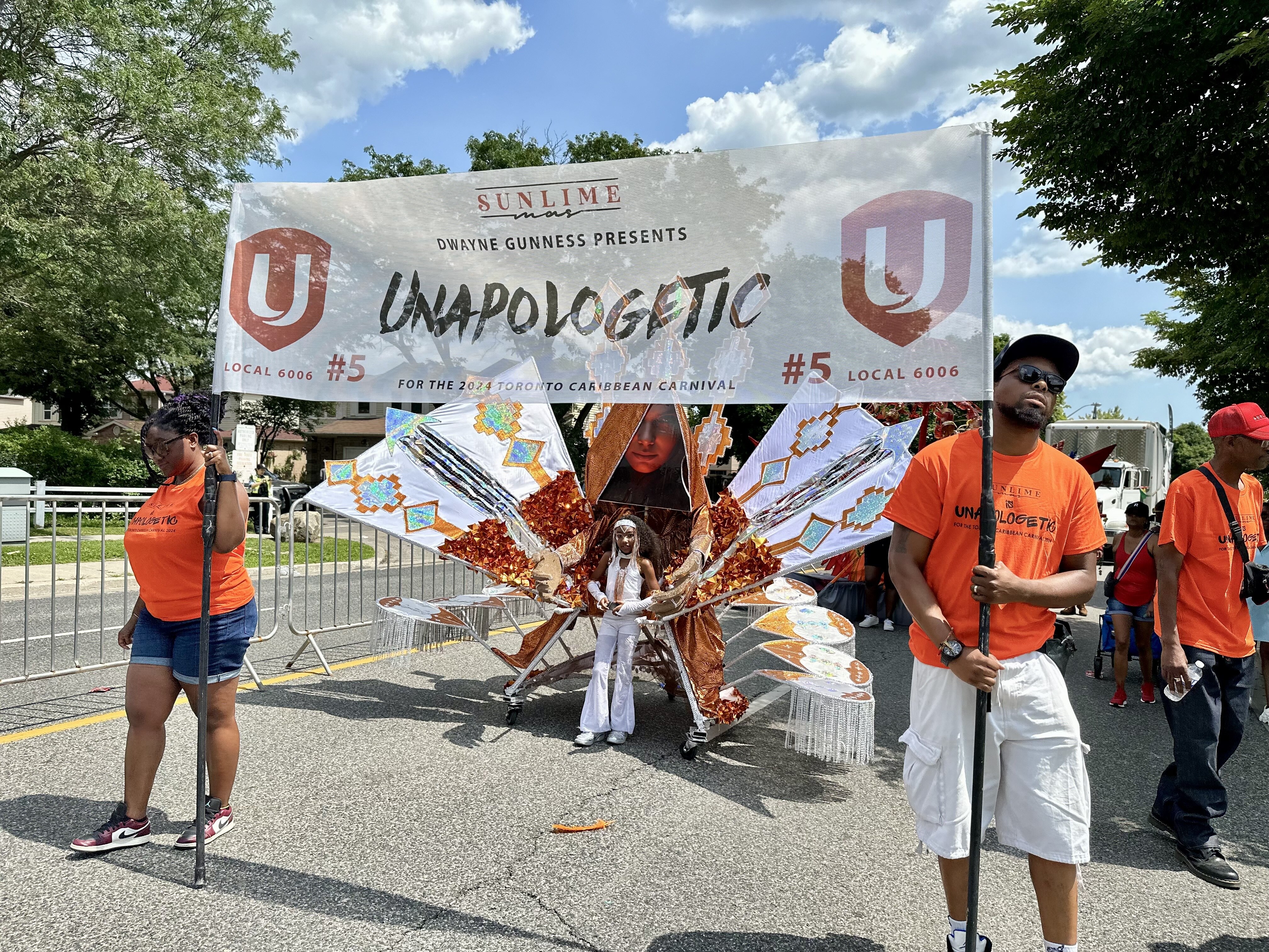 Two people wearing orange shirts carrying a Unifor banner.