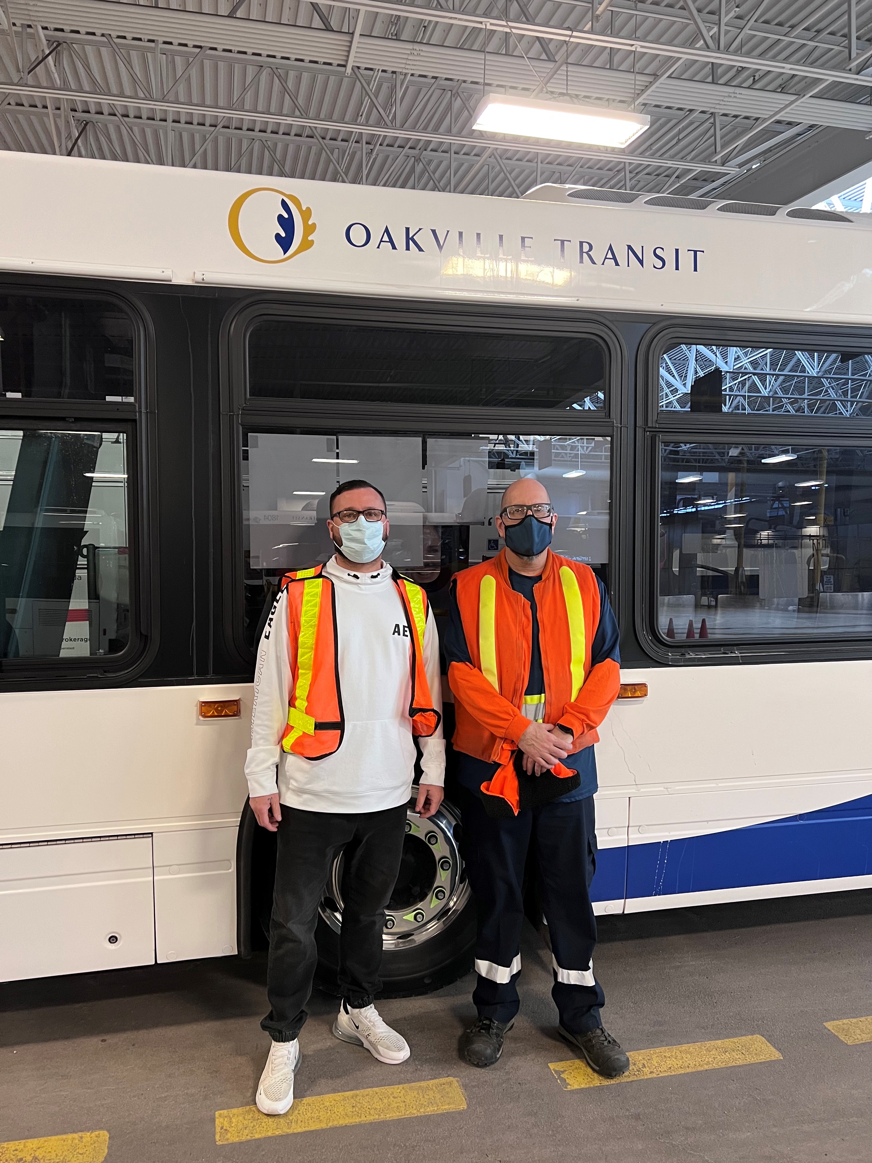 Two workers stand in front of Oakville Transit bus.