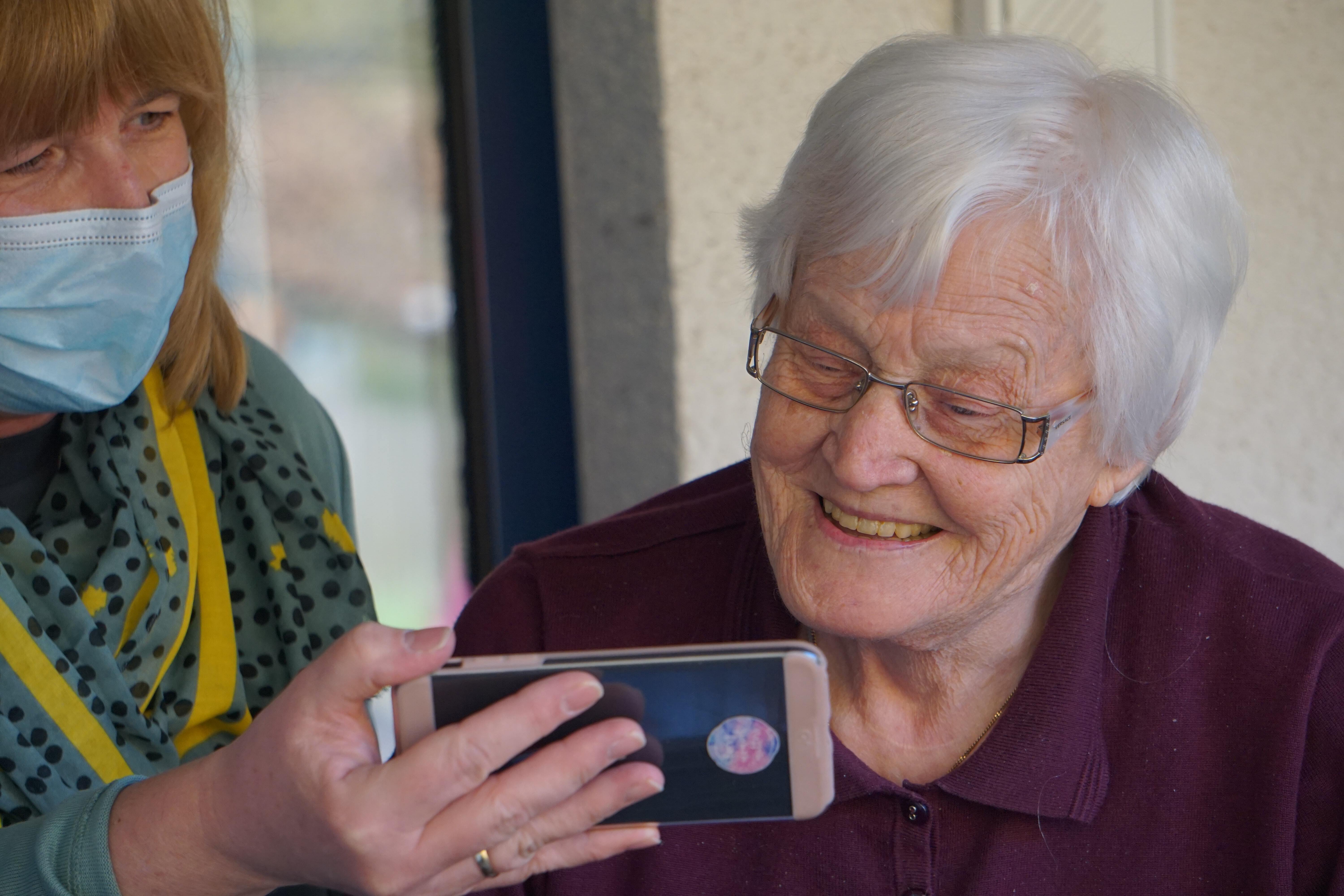 Older woman looking at a phone held by a PSW
