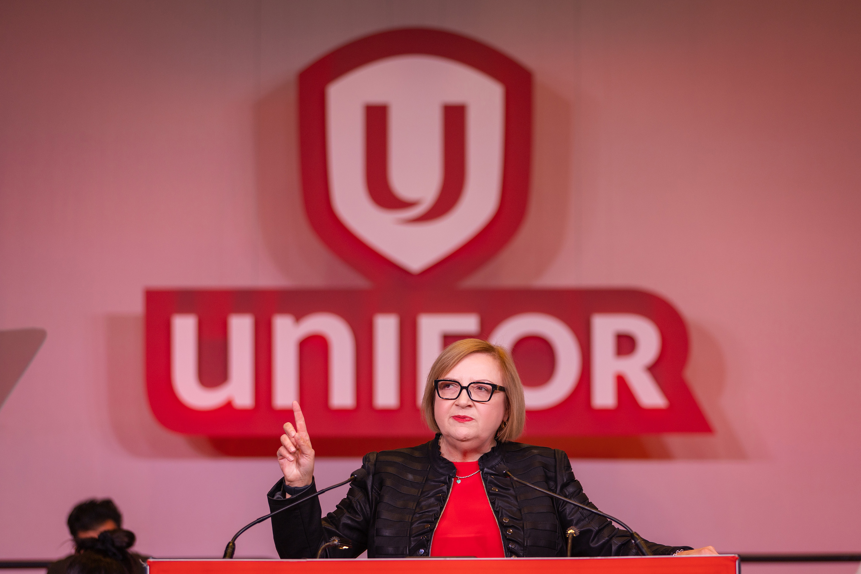 Lana Payne speaks at a mic in front of a Unifor sign