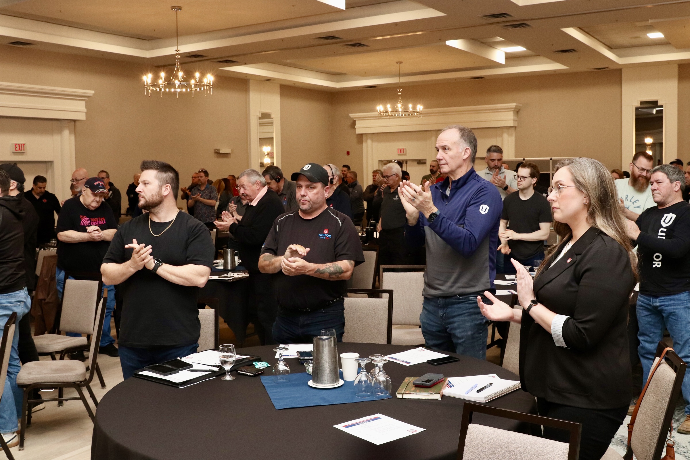 poeple standing clapping facing the front of the room